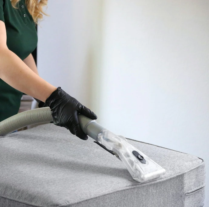 a woman in a green shirt and black gloves vacuuming a gray ottoman